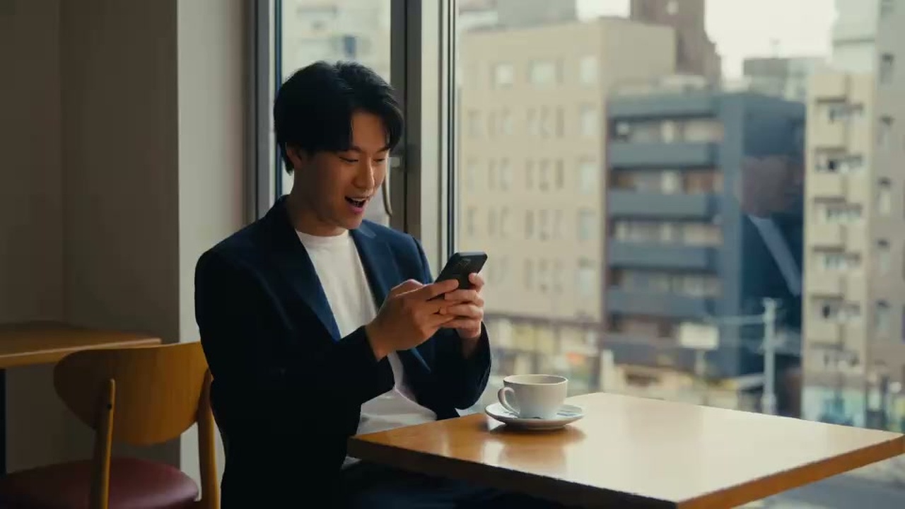 カフェの窓際でスマホを見つめ、ブラック・ブレット12年ぶりの復活告知に息を呑むファン