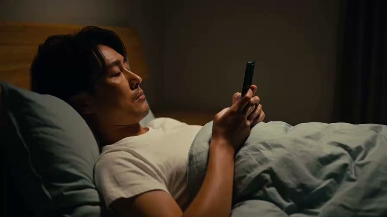 朝のベッドの中でスマートフォンを見つめて眠気に襲われる人の姿