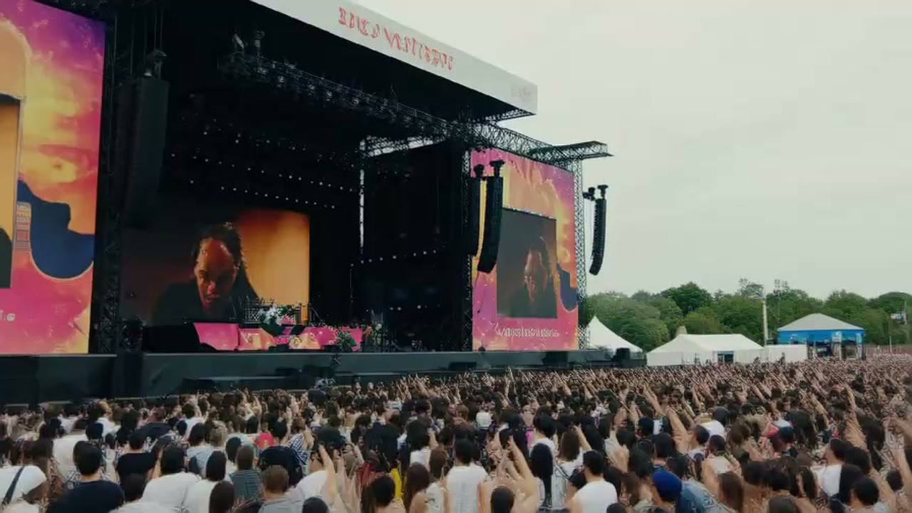 広大な野外フェスのメインステージで大観衆を前に熱唱するロックバンドのリアルライブ風景